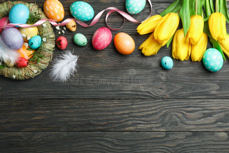 Nest with Ñolorful easter eggs, flowers and feathers on wooden background. Festive tradition. Space for text. Top view